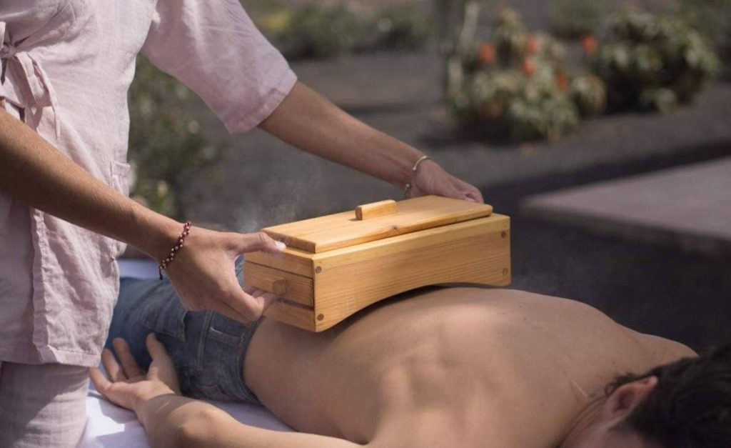 Una persona usando moxa en la zona lumbar de otra persona